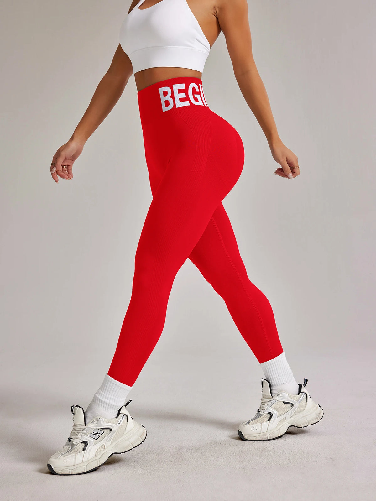 Eine Frau in roten, hochtaillierten, nahtlosen Yoga-Leggings und einem weißen Crop-Top posiert.