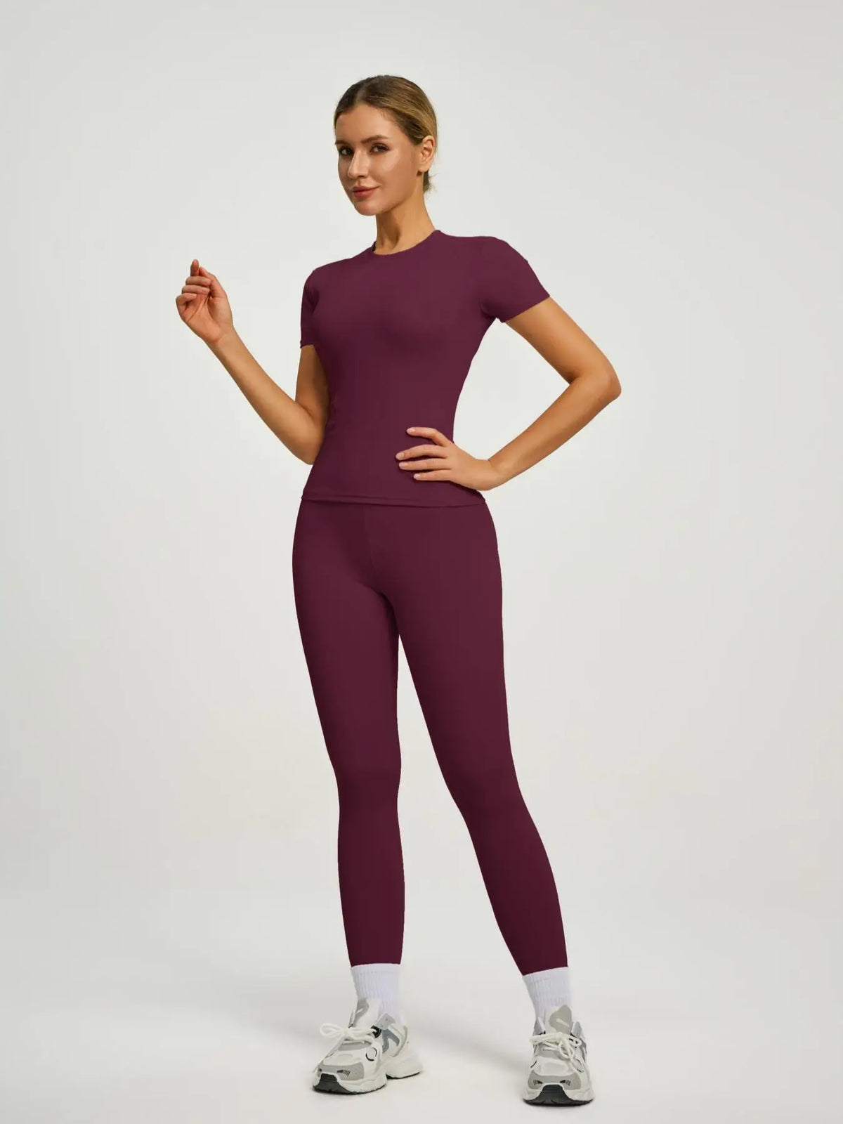 Model trägt ein sportliches Yoga-Set in tiefem Pflaumenton, bestehend aus langärmeligem Oberteil und Leggings.