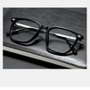 A pair of black retro anti-blue light glasses resting on a dark leather book.