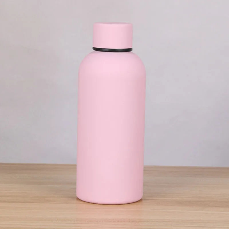 A pink double-layer vacuum thermos cup with a black lid sitting on a wooden surface.