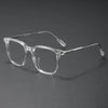 Clear acetate eyeglasses with thin metal temples resting on a dark surface.