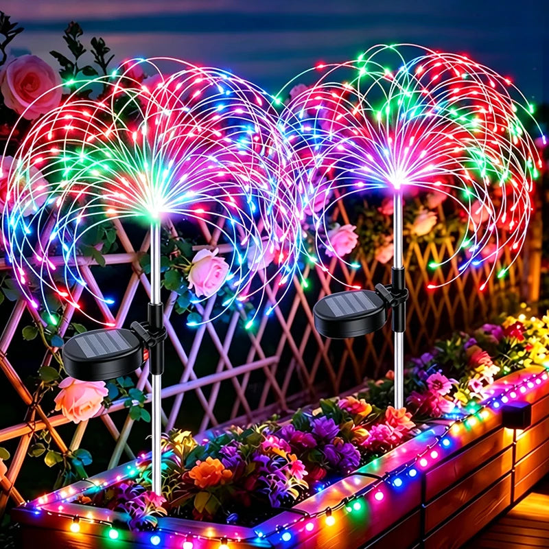 Una exhibición de fuegos artificiales de bengalas coloridas iluminando un sendero de jardín con flores y follaje.