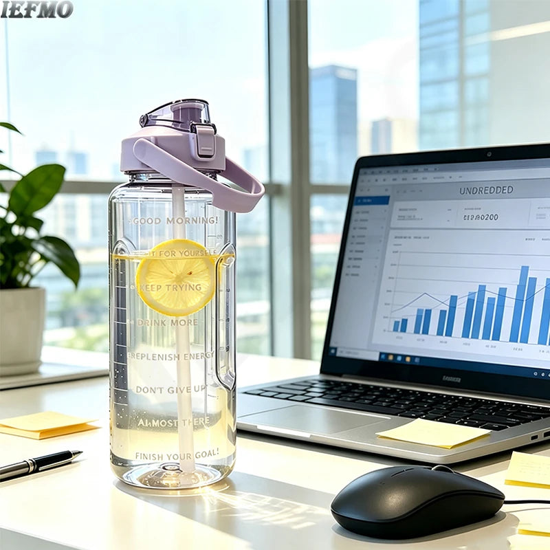 Klare Wasserflasche mit lila Verschluss und gelbem Zeitmarker auf einem Schreibtisch neben einem Laptop.