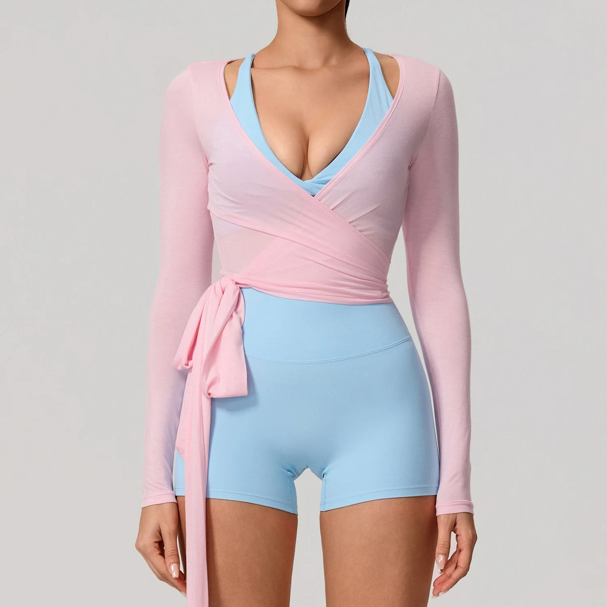 A woman models a pink long sleeve top with a blue V-neck and light blue athletic shorts.