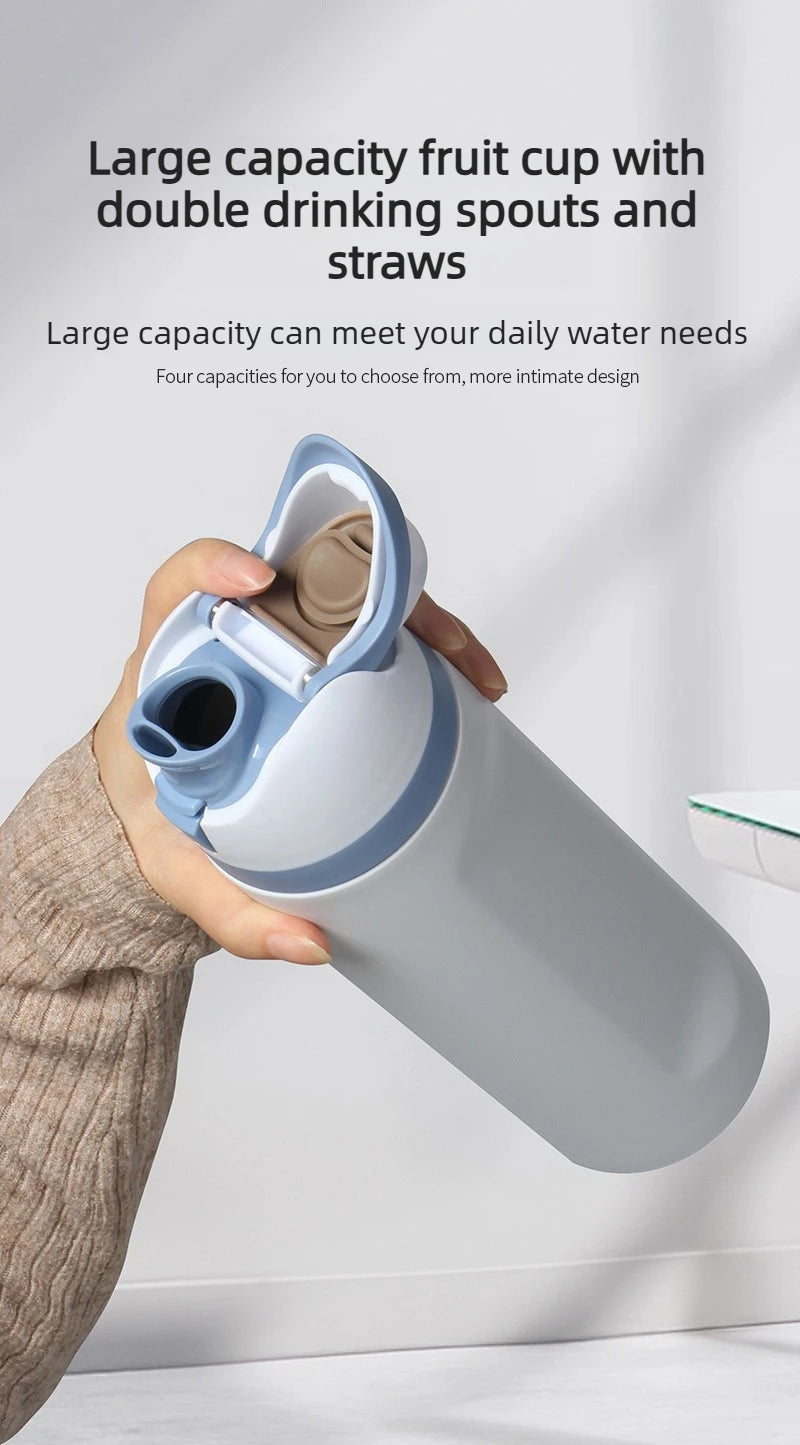 A hand holds a large capacity light blue insulated stainless steel water bottle with a dual drinking spout.
