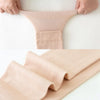 A pair of beige compression thigh high socks being held by hands, showing the texture and fit.