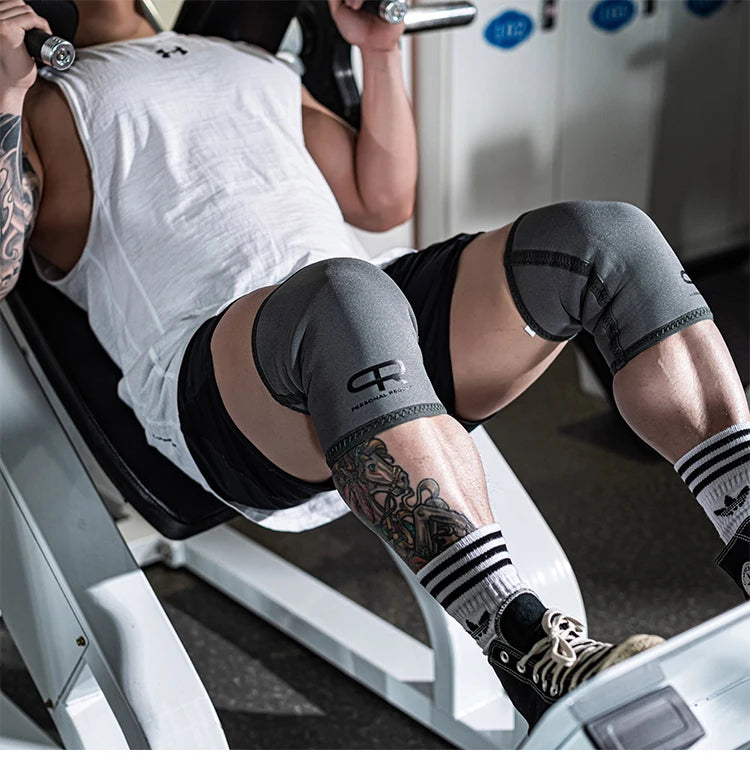 A person wearing black shorts and a white shirt is using a weight machine while wearing neoprene knee pads.