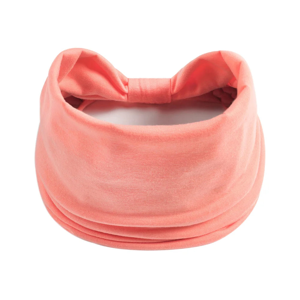 Un foulard en coton bohème couleur rose corail doux noué autour de la tête.