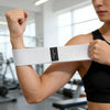 A person demonstrates using a white fabric resistance band on their forearm for a workout.