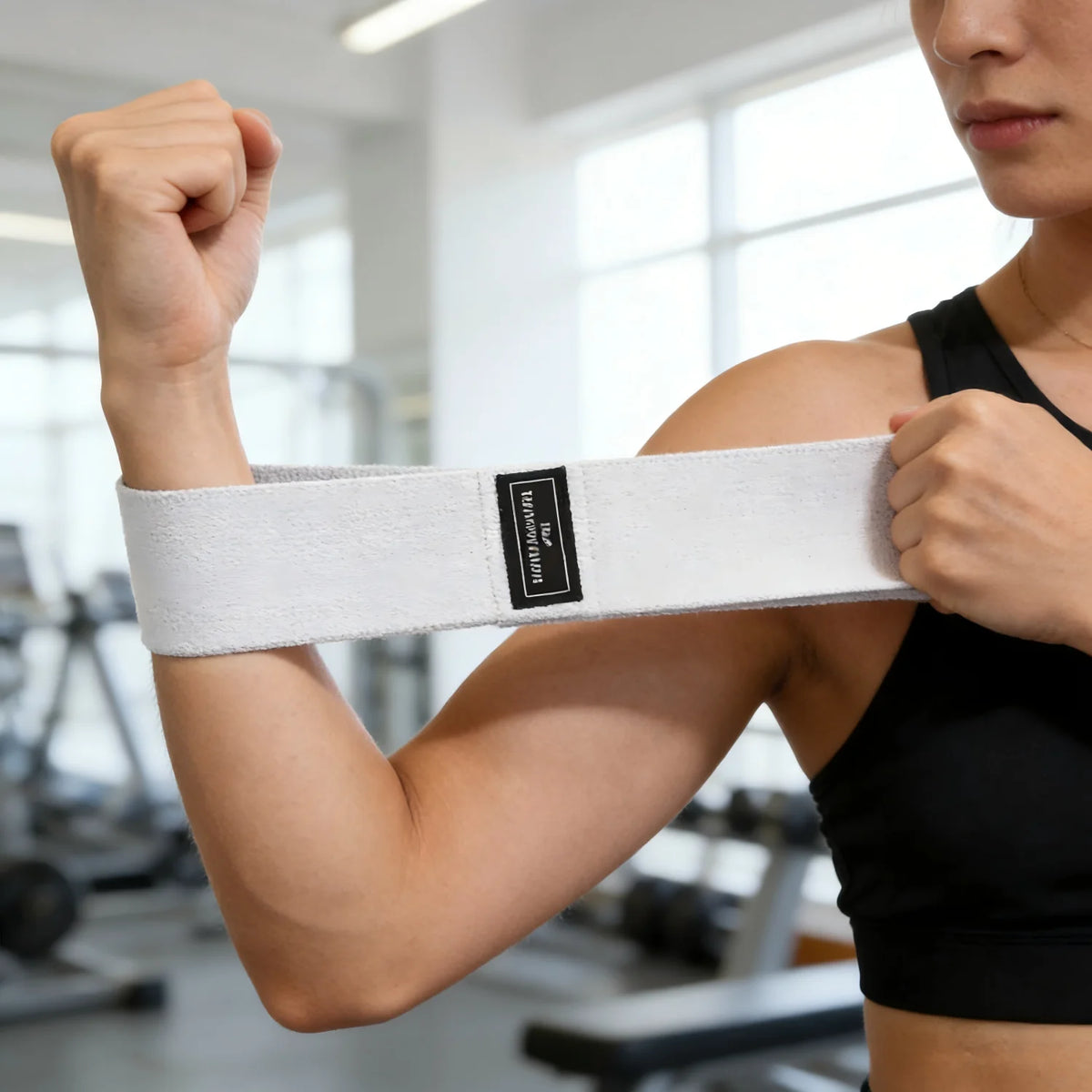 A person demonstrates using a white fabric resistance band on their forearm for a workout.