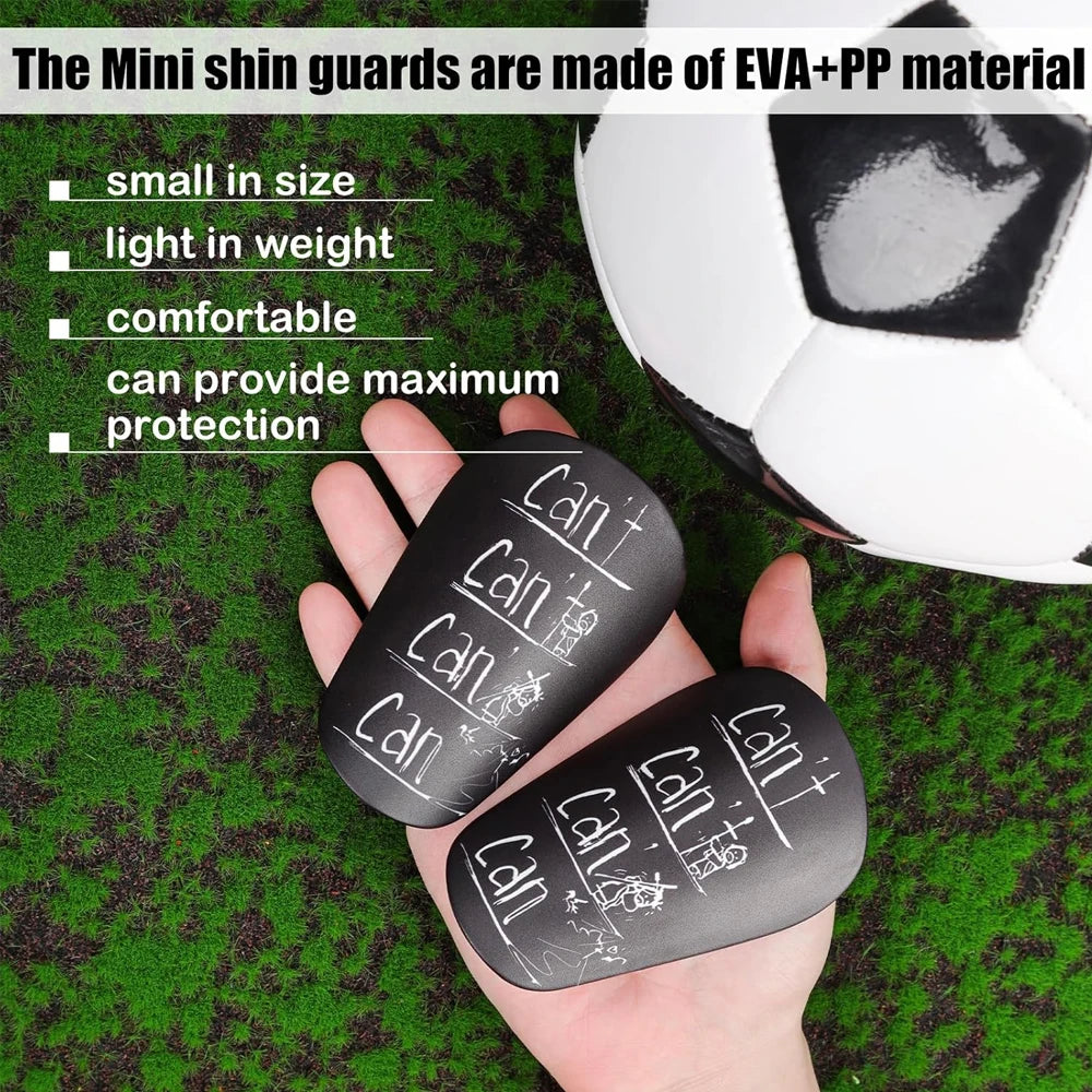 A hand holds black EVA+PP mini shin guards against a green soccer field background.