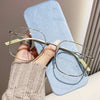A pair of thin wire-frame reading glasses rests on a light blue cloth, held by a person wearing a beige knitted sweater.
