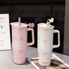 A pink and white insulated thermos mug with floral inlay details is displayed on a table.