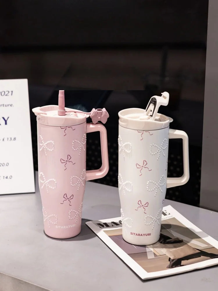 A pink and white insulated thermos mug with floral inlay details is displayed on a table.