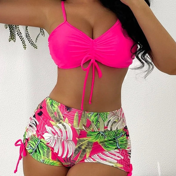 A woman models a bright pink crop top and matching floral print bikini bottoms.