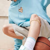 A person wearing a light blue hoodie and beige shorts is sitting next to a basketball with a knee brace strap visible on thei