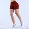 A model is wearing a terracotta-colored seamless high-waisted yoga short and white athletic shoes.