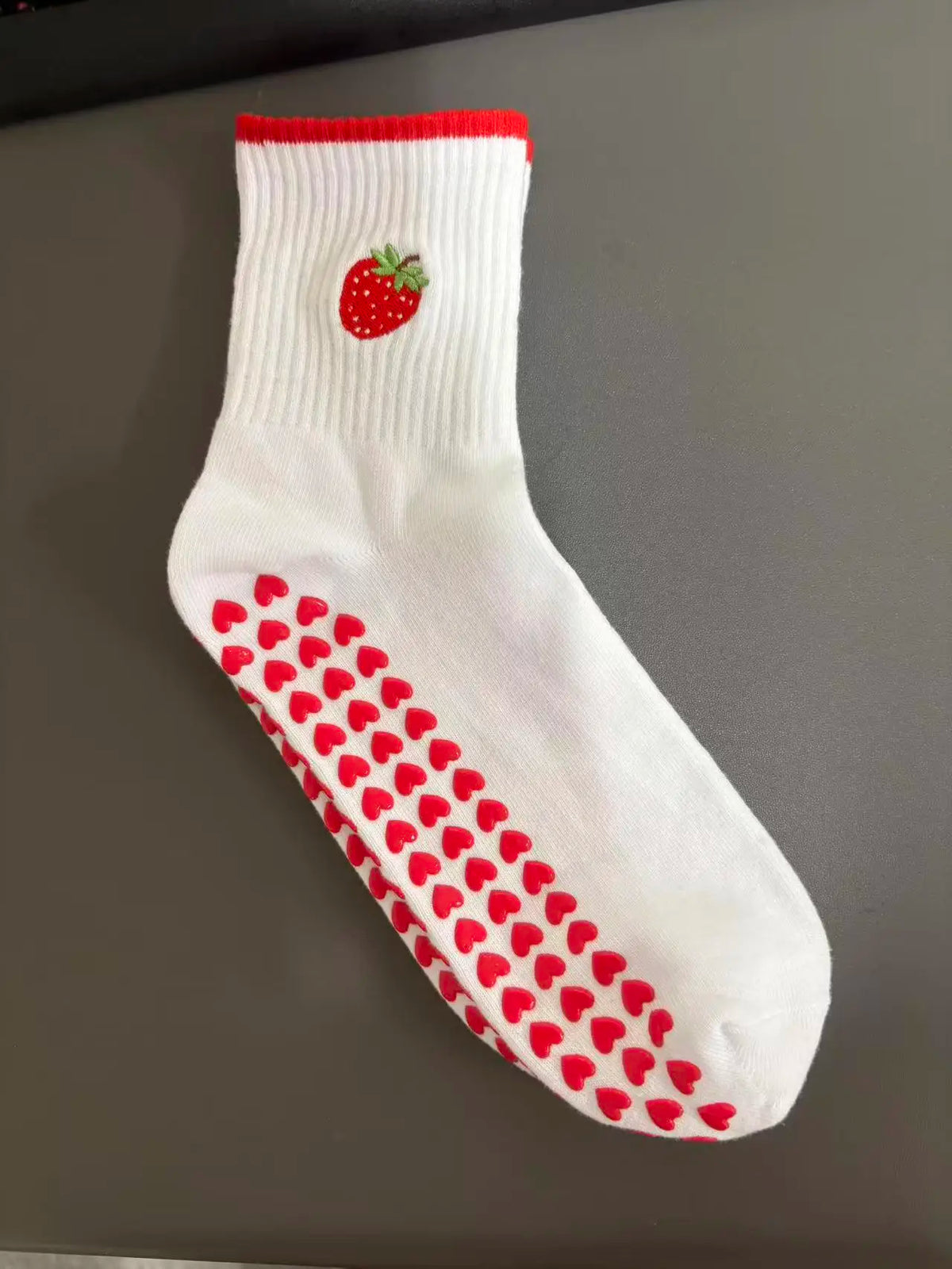 Weiße Strick-Yoga-Socken mit roter Erdbeere und Herzmuster am Fuß.