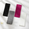 Un paquete de cuatro bandas elásticas para el cabello en negro, magenta, gris y blanco exhibidos sobre una superficie blanca.