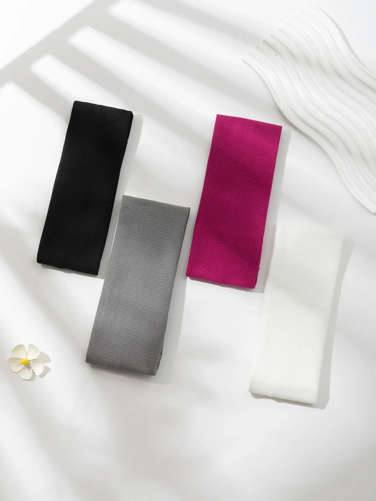 Un paquete de cuatro bandas elásticas para el cabello en negro, magenta, gris y blanco exhibidos sobre una superficie blanca.