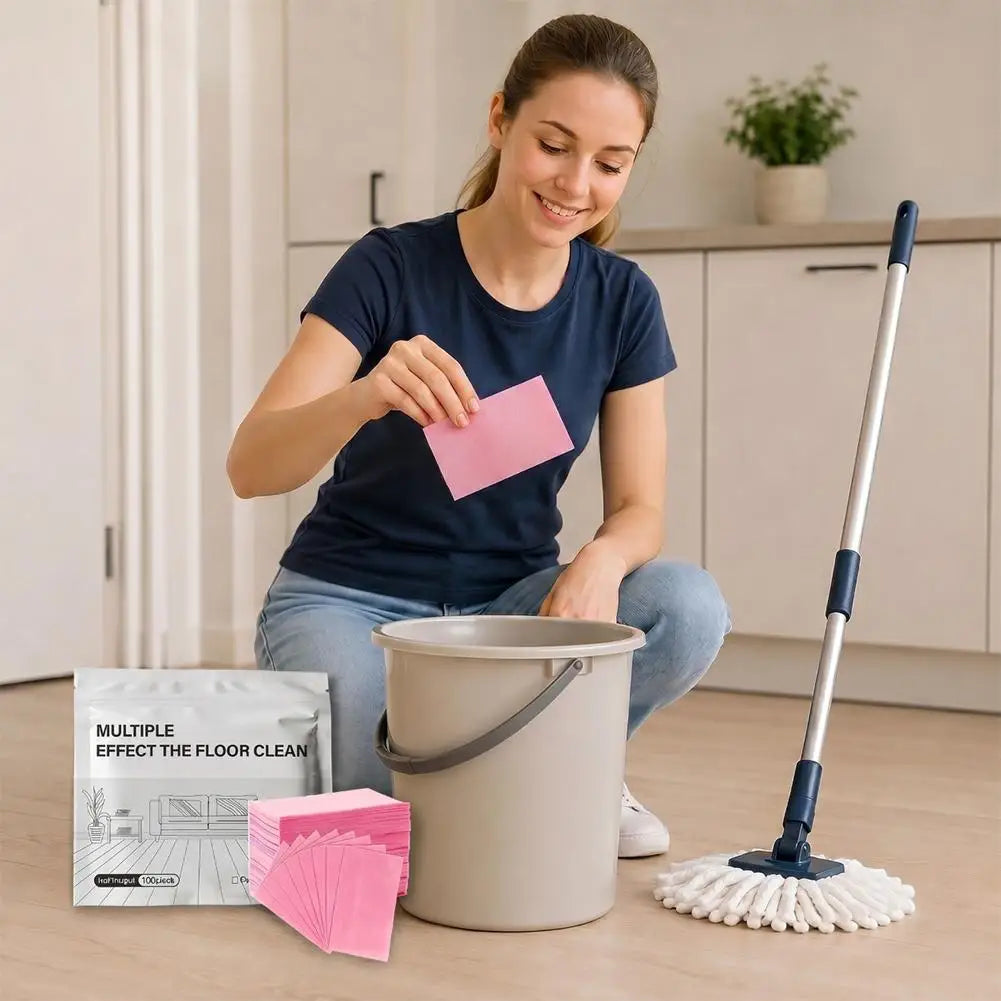 A woman is preparing to use Aroma Floor Cleaning Tablets, which are pink tablets, in a grey bucket and mop.