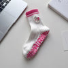 Chaussettes de yoga blanches à rayures roses et broderie de cœur, posées sur une surface blanche.