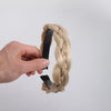 A hand is braiding a light blonde hair extension into a twisted braid using a black elastic band.