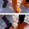 A close-up of a person's feet wearing bright orange waterproof boots in the snow.
