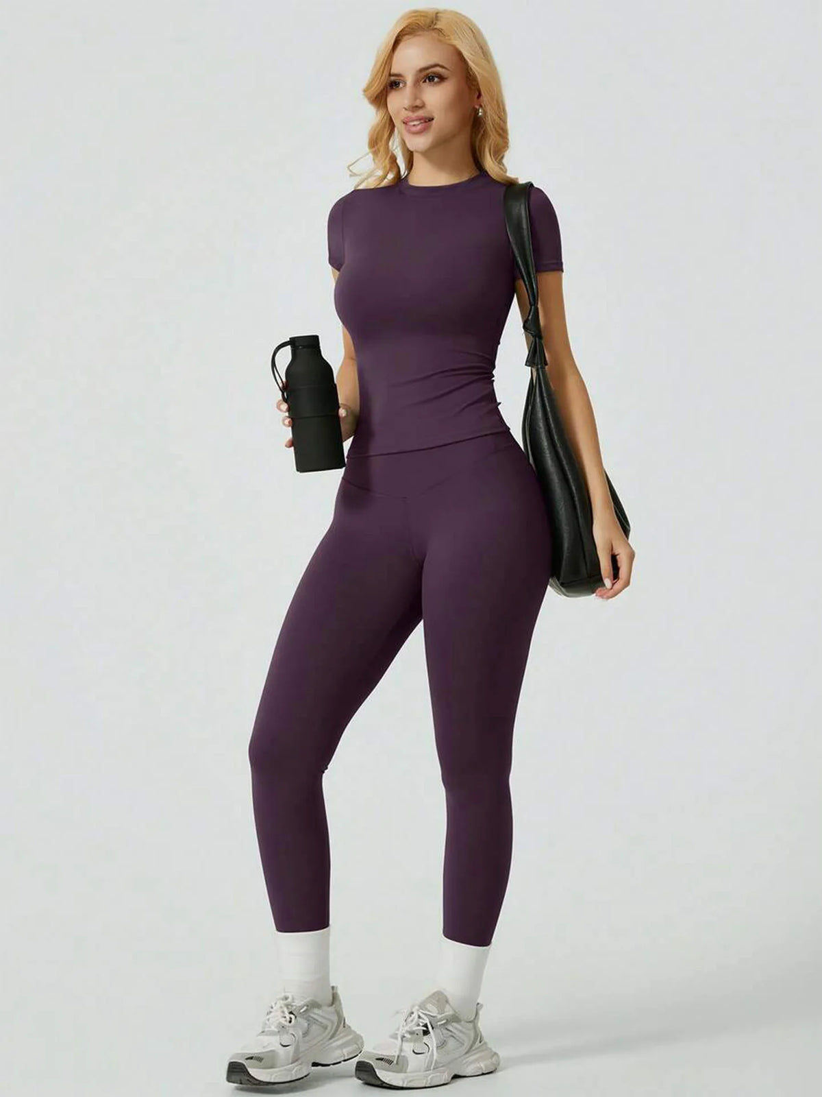 Eine Frau modelliert ein lila Zweiteil-Yoga-Set mit hohen Leggings und einem kurzen Oberteil.