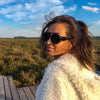 A woman wearing black retro steampunk goggles sunglasses outdoors with a bright blue sky and green field background.
