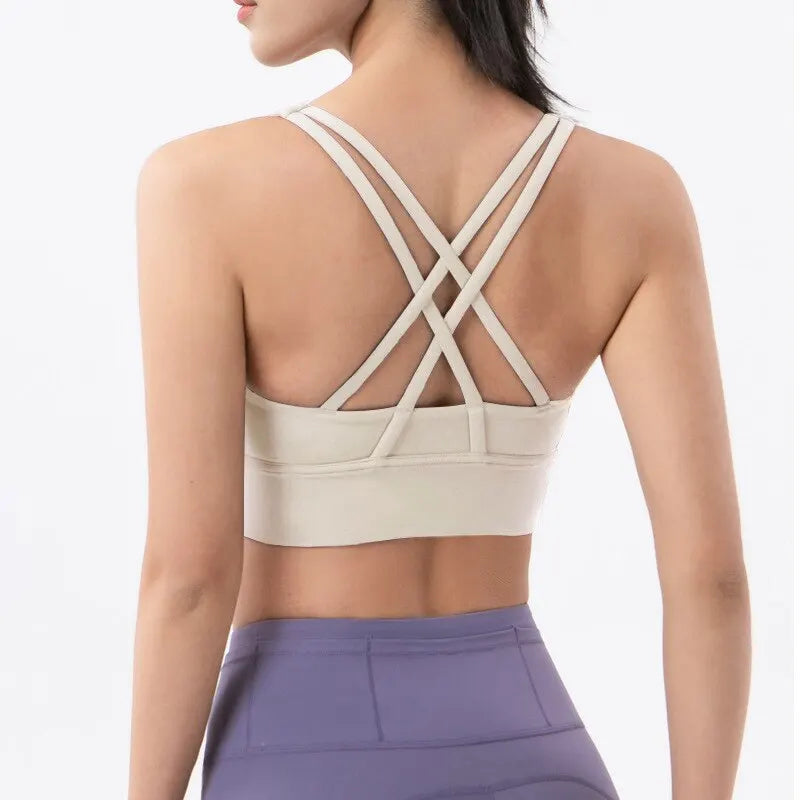 Eine Frau trägt ein beiges atmungsaktives Nylon-Yoga-Sports-BH und lila Sporthosen, von hinten gezeigt.