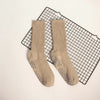 Pair of beige knitted mid-calf yoga and pilates socks displayed on a black grid mat.