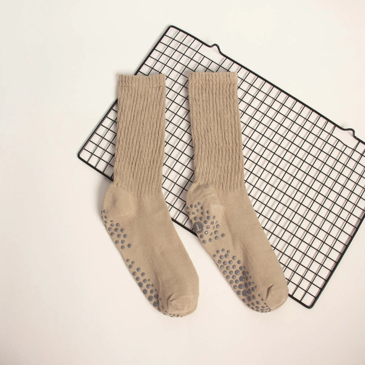 Pair of beige knitted mid-calf yoga and pilates socks displayed on a black grid mat.