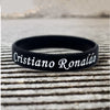 Schwarzes Silikonarmband mit dem Namen Cristiano Ronaldo auf einer Holzoberfläche.