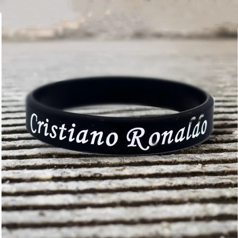 Schwarzes Silikonarmband mit dem Namen Cristiano Ronaldo auf einer Holzoberfläche.