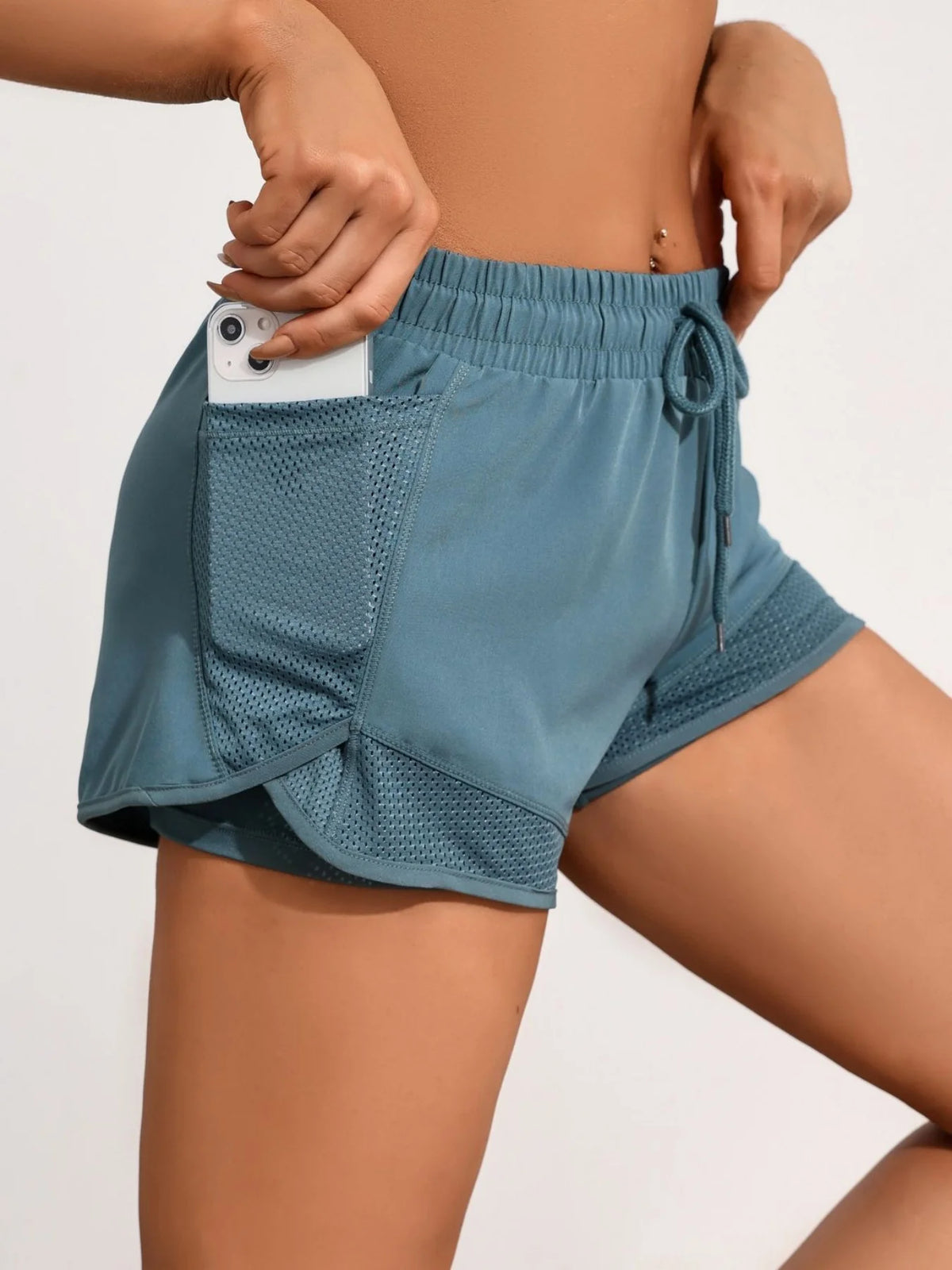 A model wears teal athletic shorts with mesh pockets and a drawstring detail.