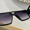 A close-up view of black geometric fashion sunglasses with clear rhinestone detailing.