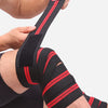 A person is applying black and red high-compression knee wraps to their leg for weightlifting.