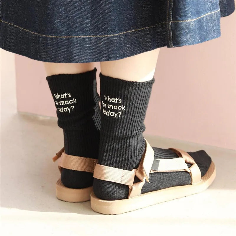 A pair of black embroidered cotton socks worn with a denim skirt and light-colored sandals.