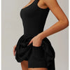 Model in a black performance tennis dress with a sleeveless top and ruffled skirt.