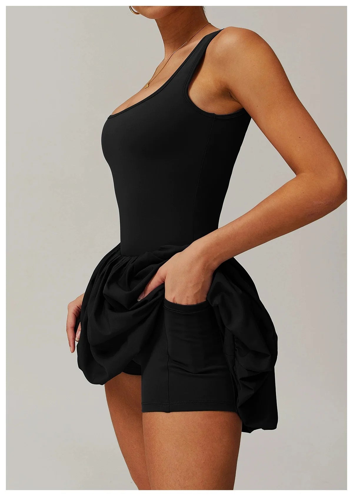 Model in a black performance tennis dress with a sleeveless top and ruffled skirt.