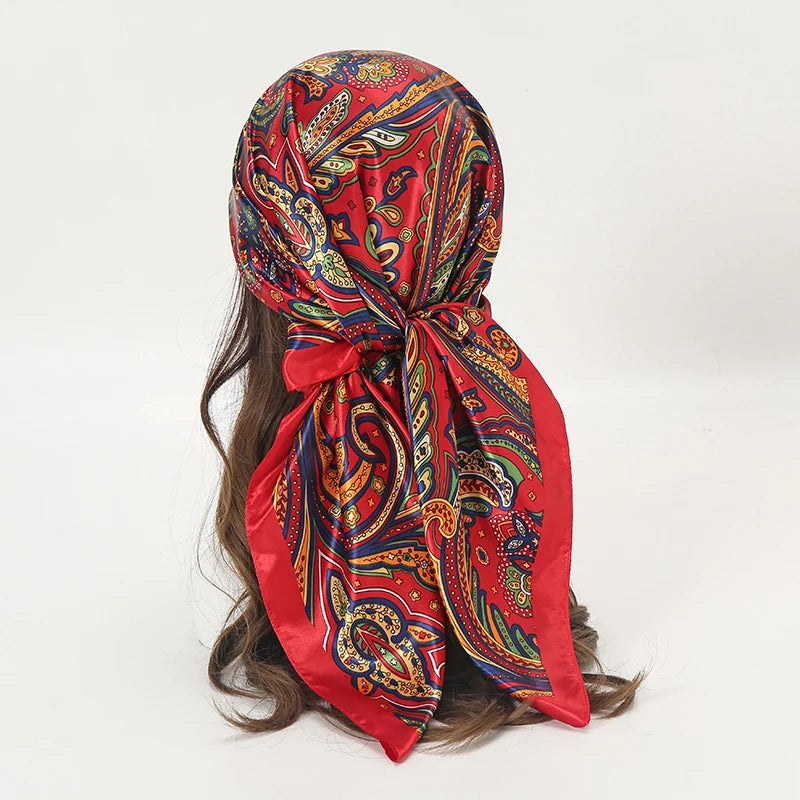 A vibrant red satin square scarf with intricate paisley patterns tied around a person's hair.