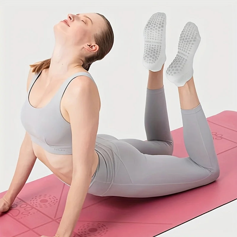 A woman performing a stretch on a pink mat wearing gray Pilates socks.