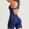 A woman wearing a navy blue, form-fitting, backless fitness jumpsuit.