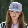 A young woman wearing a light purple baseball cap with the text GOD ONE MORE on it and a white shirt.