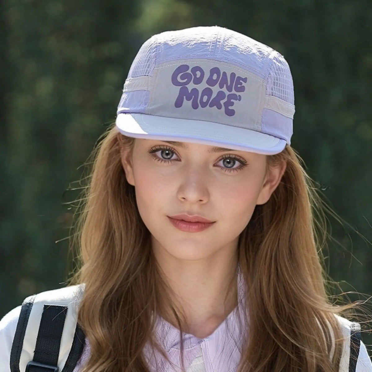 A young woman wearing a light purple baseball cap with the text GOD ONE MORE on it and a white shirt.