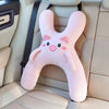 Un coussin de cou car en forme de porc rose posé sur un siège de voiture de couleur claire.