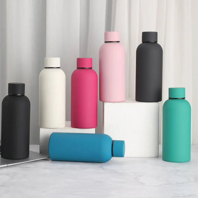 A collection of double-layer vacuum thermos cups in pink, black, and teal colors displayed on a white surface.