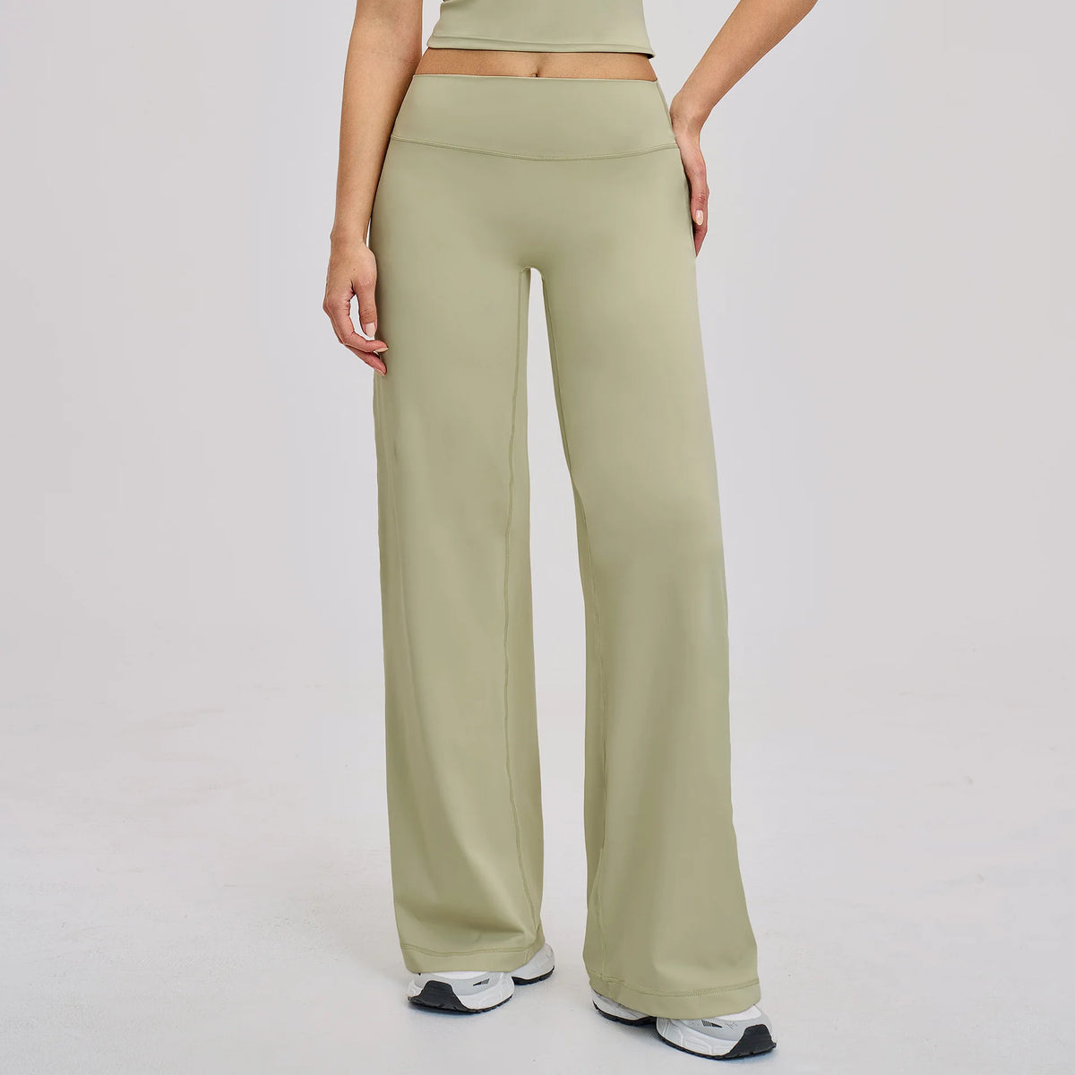 A woman wearing light olive green high-waist flared yoga pants and a matching crop top.