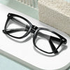 A pair of black anti-blue light gaming glasses resting on a white surface next to a textured block.